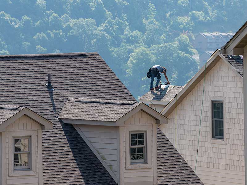 Worker on a large residential roof installing the last of the light brown shingles the roof will have